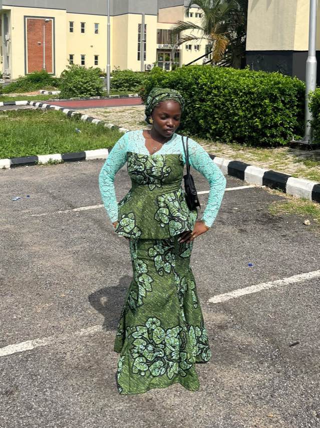 A woman in a green and gold lace gown with a matching headwrap