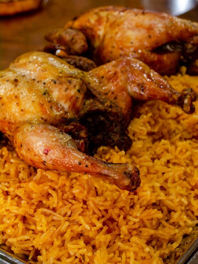 A tray of jollof rice topped with two whole roasted chickens